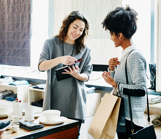 Two smiling ladies, one a business owner processing a sale with a credit card and her iPad.